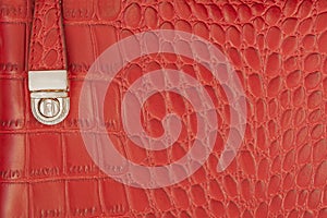 Texture of red handbag from genuine leather with embossed under the skin of reptile with metal lock clasp close up