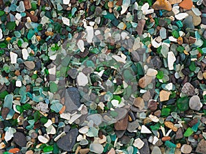 The texture of a stone beach with many pieces of colored glass