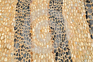 Texture stone wall road from small round oval stones abstract lines laid out patterns natural old yellow black brown background