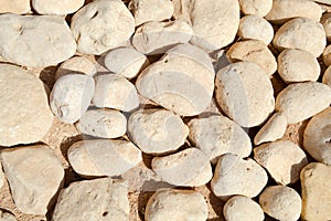 Texture of a stone wall, roads from large round and oval stones with sand with seams of natural old yellow black brown. background