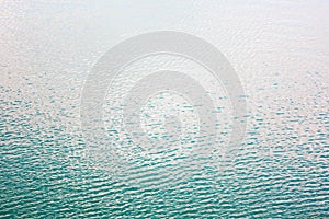 Texture of transparent clear surface of turquoise azure water with small ripples fish and sun reflections textured with waves