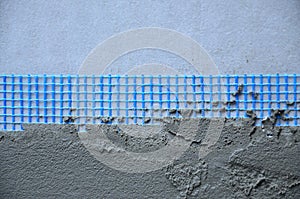 The texture of the wall, covered with gray foam polystyrene plates, covered with a blue reinforcing mesh and covered with a mixtu