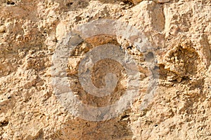 texture of the wall is made of yellow sandy friable old rotten stone of rock with shards, holes and layers. The background.