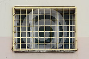 The texture of the wall of a residential building with a window that is protected by a metal grill. Old method of protecting hous