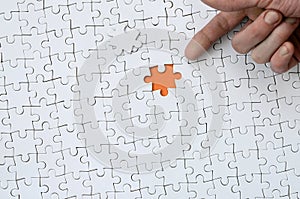 The texture of a white jigsaw puzzle in the assembled state with one missing element, forming an orange space, pointed to by the