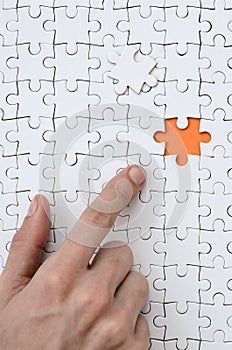 The texture of a white jigsaw puzzle in the assembled state with one missing element, forming an orange space, pointed to by the