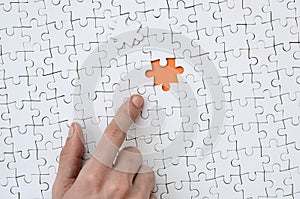 The texture of a white jigsaw puzzle in the assembled state with one missing element, forming an orange space, pointed to by the
