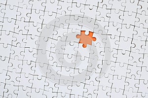 The texture of a white jigsaw puzzle in an assembled state with one missing element forming an orange space