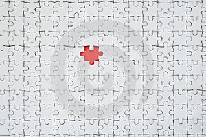 The texture of a white jigsaw puzzle in an assembled state with one missing element forming a red space