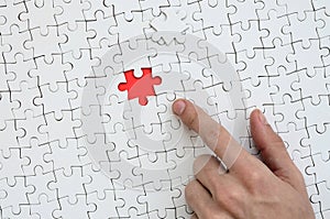 The texture of a white jigsaw puzzle in the assembled state with one missing element, forming a red space, pointed to by the finge