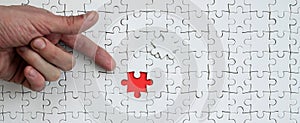The texture of a white jigsaw puzzle in the assembled state with one missing element, forming a red space, pointed to by the finge