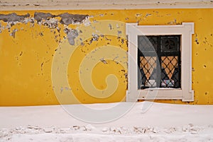 Texture of a yellow wall with a window surrounded by snow