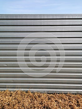 A textured background with a metal gray fence with horizontal stripes - stiffeners, in front of which is dry yellow beige grass