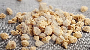 Textured chunks of organic dehydrated soybeans fall on a rough jute surface