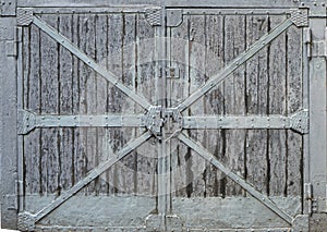 Textured doors of an old warehouse. Old wooden gate with metal inserts.