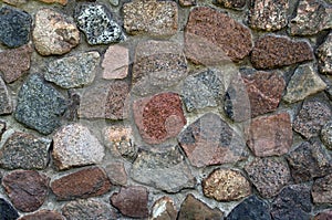 Textured fragment of the granite stone brown-gray facade of the wall