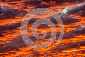 Textured moody clouds, glowing red and orange in the setting sun