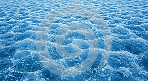 A textured surface of blue ice with a wave-like pattern, reflecting light and creating photo