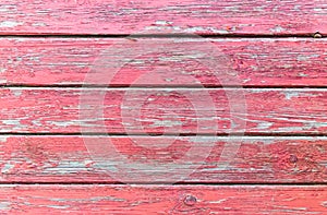 Textured surface of a horizontal wooden boards with a peeling and cracked layer of red paint. Old painted wood planks, aged