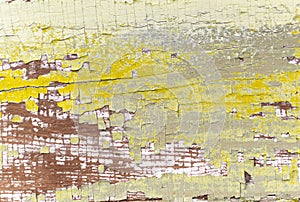 Textured surface of a old painted wooden board with a peeling and cracked layer of yellow and white paint closeup.