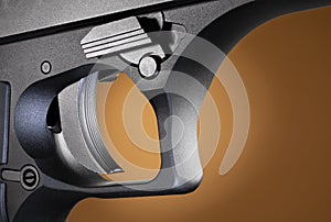 Textured trigger on a metal framed semi automatic handgun with a brown background