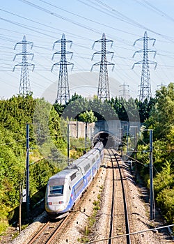 A TGV Duplex high-speed train is entering a tunnel under a row of transmission towers