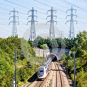 A TGV Duplex high-speed train is entering a tunnel under a row of transmission towers