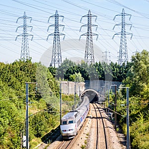 A TGV high-speed train is entering a tunnel under a row of transmission towers