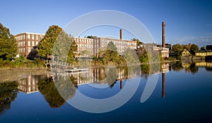 A 19th century textile mill has been renovated for modern use, seen reflected in the neighboring river photo