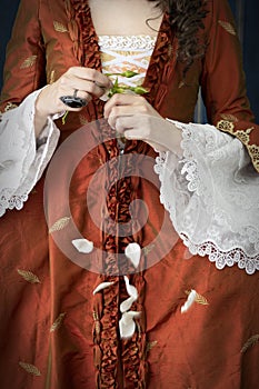 An 18th-Century woman wearing an a la Francaise gown crushing a white rose photo