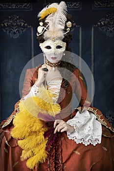 An 18th-Century woman wearing an a la Francaise gown holding a mask photo