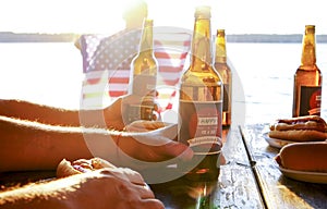 Holiday composition with multiple bottles of beer and hot dogs, American flag. Group of people celebrating Independence day of USA