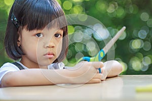 Thai Asian girl,aged 4 to 6 years old, looks cute, sitting outdoors in the garden Holding scissors in her hand Eyes staring