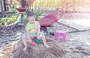 Thai baby boy palying on pile of sand with toy