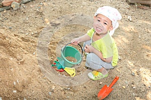 Thai baby boy palying on  pile of sand with toy and plastic fork