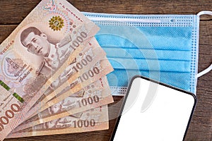 Thai baht banknotes money with protective mask and smart phone on desk ,covid-19 cash subsidy concept