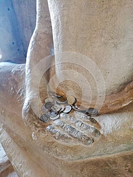 Thai Baht coins on the hand Buddha statue, Thailand