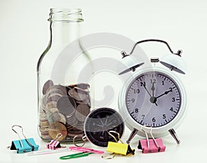 Thai bath coins into clear glass jar with white alarm clock isolated on white background Concept finance and business banking