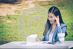 Asian business woman in office uniform Talking on the cell phone with the customer sitting on the table in the park. With a smilin