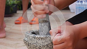 Thai chilli and garlic pounding in stone mortar with pestle. Woman preparing sauce for thai soup tom yam. Close Up. 4k