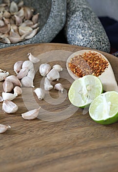 Thai cooking kitchen concept, garlics in stone mortar beside with pestle and piece of lime and dry chilly on wooden spoon