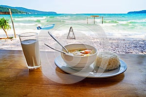 Thai cuisine. A plate of soup with coconut milk and boiled rice on the table against the beautiful sea landscape. Breakfast at the