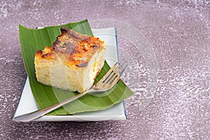 Thai custard cake or Khanom mo kaeng in Thai on banana leaf and spoon on a white plate with a stone background. Egg custard with