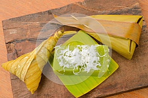 Thai dessert sticky rice wrapped in banana leaf on wood background.
