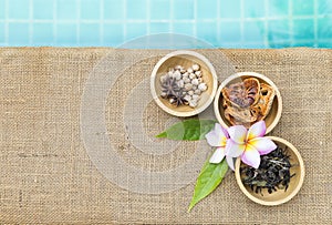 Thai dry herbs in round wooden bowl with Plumeria flower on hessian fabric background