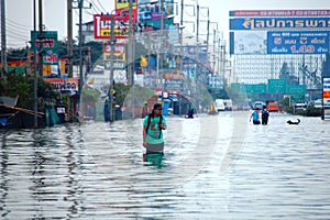 Thai family people natural disaster victims walking wading in water on street of alley while water flood road go receive goods