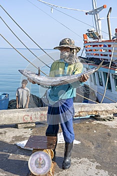 Thai fisherman shows caught fish on the pier near fishing boat on the island Koh Phangan, Thailand