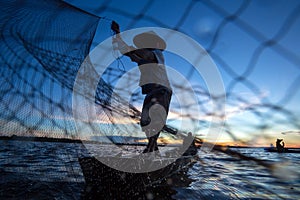 Thai fisherman on wooden boat casting a net