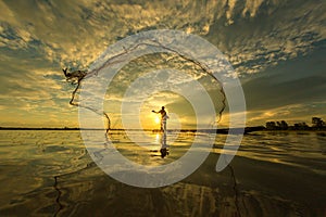 Thai fisherman on wooden boat casting a net