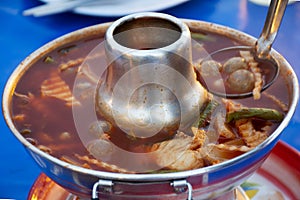 Thai food Sour soup and orange curry with spawn of giant catfish fish and mixed veggies in hot pot on table in local restaurant